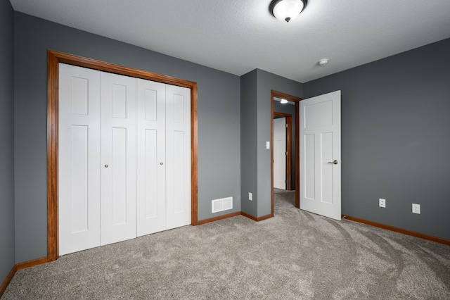 unfurnished bedroom with a textured ceiling, light carpet, visible vents, baseboards, and a closet