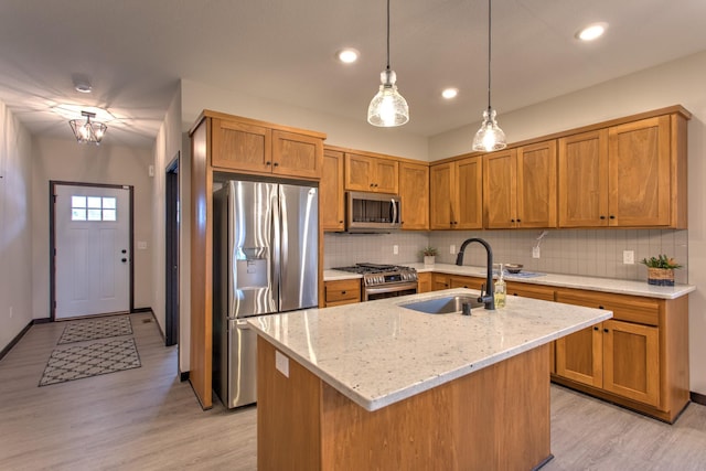 kitchen featuring light stone countertops, pendant lighting, a kitchen island with sink, appliances with stainless steel finishes, and sink