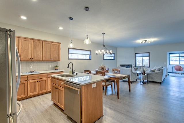 kitchen with a kitchen island with sink, appliances with stainless steel finishes, pendant lighting, sink, and backsplash