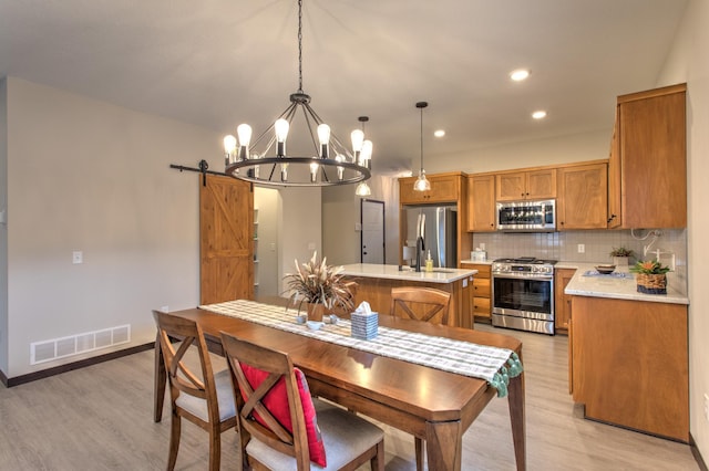 dining space featuring sink, an inviting chandelier, light wood-type flooring, and a barn door