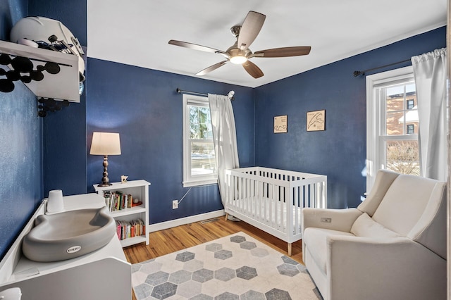 bedroom featuring ceiling fan, a crib, and hardwood / wood-style floors