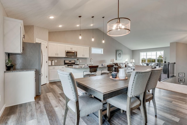 dining room featuring an inviting chandelier, light wood-type flooring, high vaulted ceiling, and sink