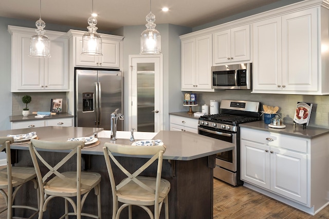 kitchen with pendant lighting, white cabinets, appliances with stainless steel finishes, backsplash, and light hardwood / wood-style flooring