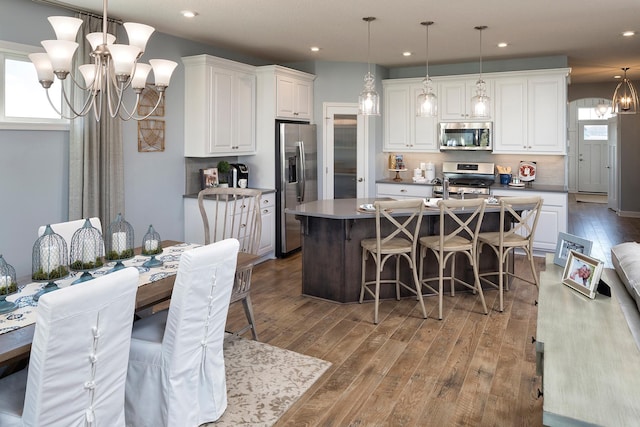 kitchen featuring decorative light fixtures, white cabinetry, stainless steel appliances, and an island with sink