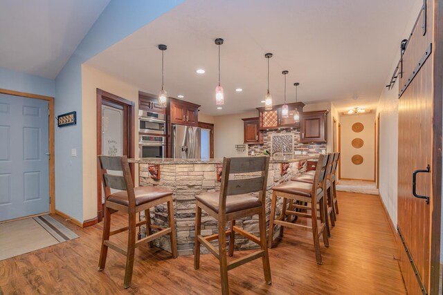 kitchen featuring tasteful backsplash, stainless steel fridge, hanging light fixtures, kitchen peninsula, and light wood-type flooring