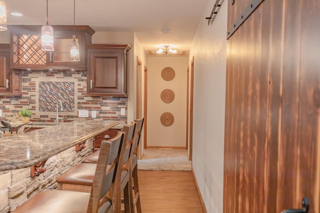 kitchen featuring light stone counters, backsplash, light hardwood / wood-style floors, and pendant lighting