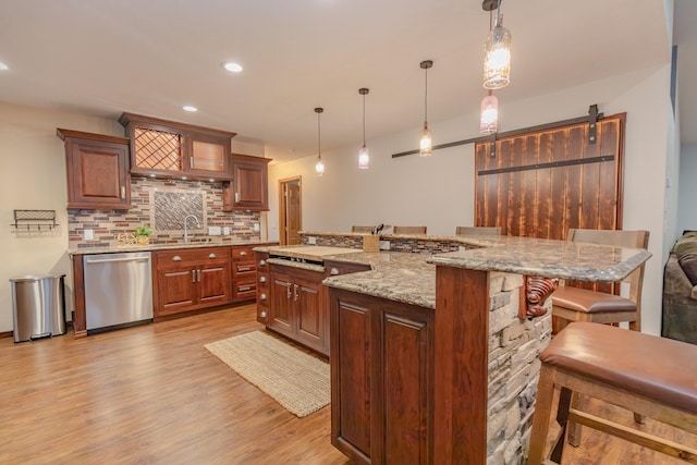 kitchen featuring a barn door, stainless steel dishwasher, backsplash, and decorative light fixtures