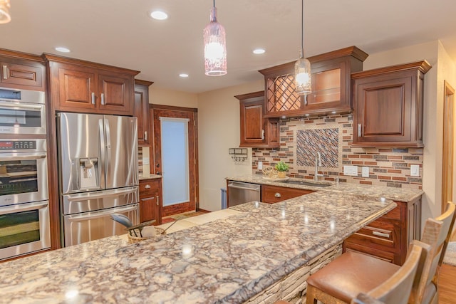 kitchen with sink, a breakfast bar, appliances with stainless steel finishes, backsplash, and decorative light fixtures