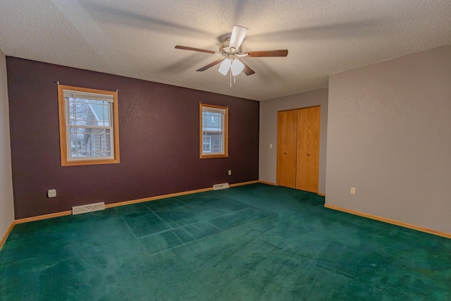 unfurnished room with ceiling fan, a textured ceiling, and dark colored carpet