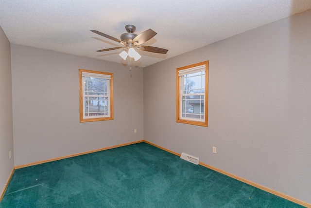 unfurnished room with ceiling fan, dark carpet, and a textured ceiling