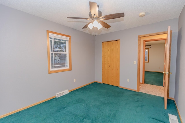 unfurnished bedroom with ceiling fan, a closet, a textured ceiling, and dark colored carpet