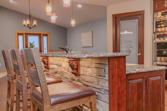 interior space featuring vaulted ceiling, double oven, pendant lighting, light stone countertops, and light hardwood / wood-style floors