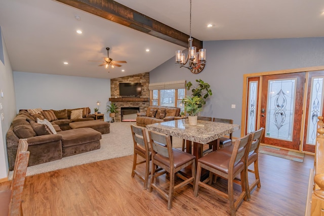 dining space with a fireplace, ceiling fan with notable chandelier, light hardwood / wood-style flooring, and vaulted ceiling with beams