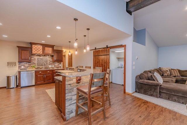 kitchen featuring a kitchen bar, washer / dryer, decorative light fixtures, dishwasher, and a barn door