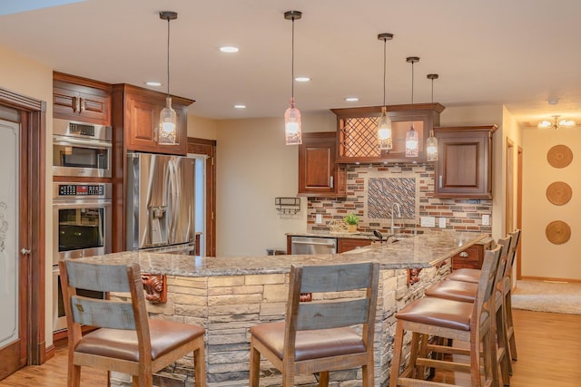 kitchen with a breakfast bar, light stone counters, appliances with stainless steel finishes, kitchen peninsula, and pendant lighting