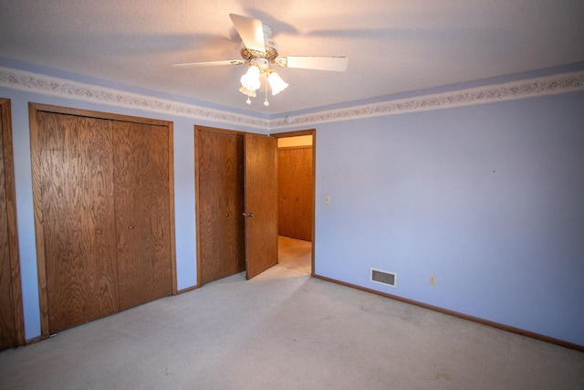 unfurnished bedroom with two closets, ceiling fan, and light colored carpet