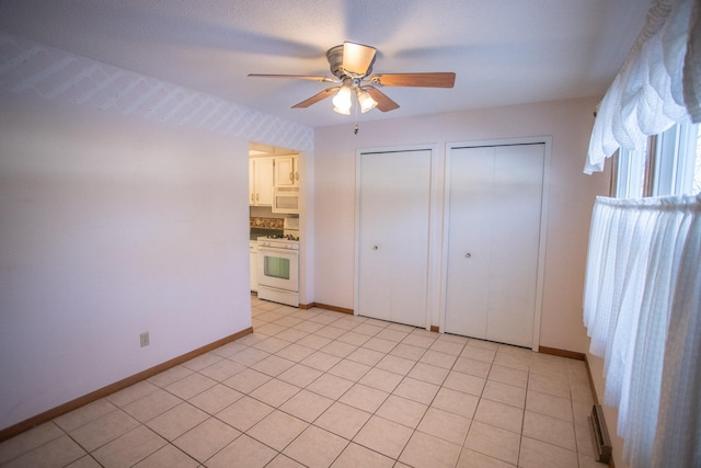 unfurnished bedroom featuring ceiling fan, light tile patterned floors, and multiple closets