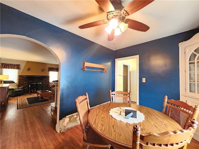 dining area featuring hardwood / wood-style flooring, a fireplace, arched walkways, and a ceiling fan