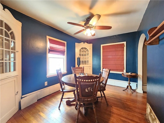 dining space featuring ceiling fan, arched walkways, hardwood / wood-style flooring, and baseboards