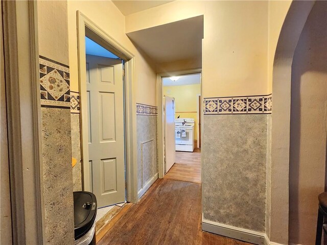 hall featuring tile walls, arched walkways, and wood finished floors