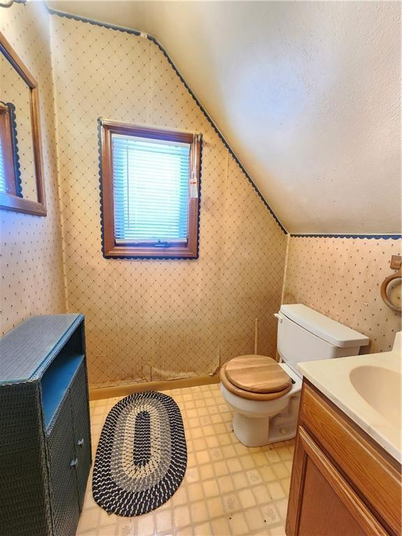 bathroom featuring lofted ceiling, wallpapered walls, toilet, and vanity