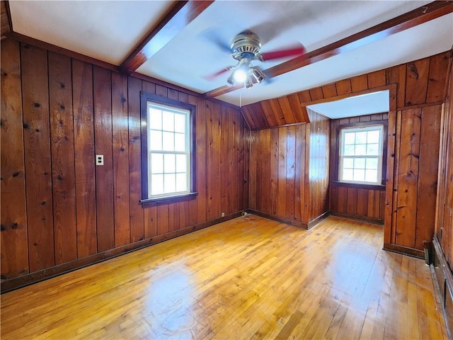 unfurnished room with beamed ceiling, light wood-type flooring, a wealth of natural light, and a ceiling fan