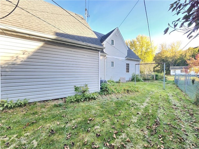 view of side of property with a yard, roof with shingles, and fence