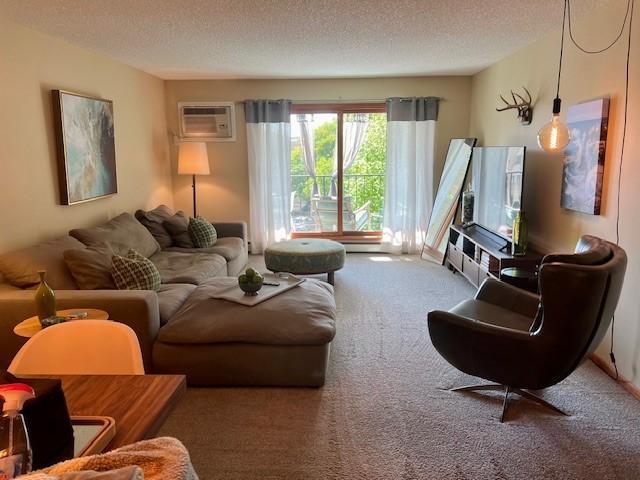 living room with a textured ceiling, carpet, and a wall mounted AC