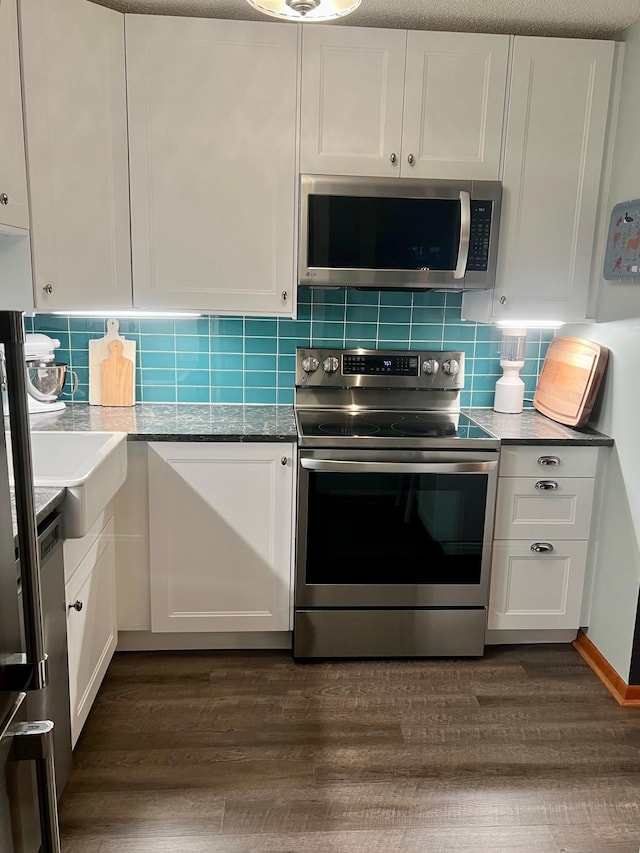 kitchen with appliances with stainless steel finishes, dark hardwood / wood-style flooring, white cabinets, and tasteful backsplash