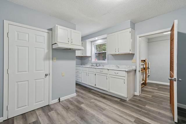 kitchen with sink, white cabinets, a textured ceiling, and light wood-type flooring