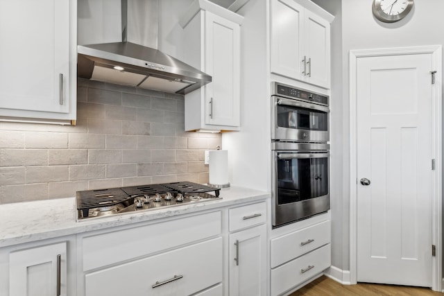 kitchen featuring white cabinetry, appliances with stainless steel finishes, tasteful backsplash, light stone countertops, and wall chimney exhaust hood