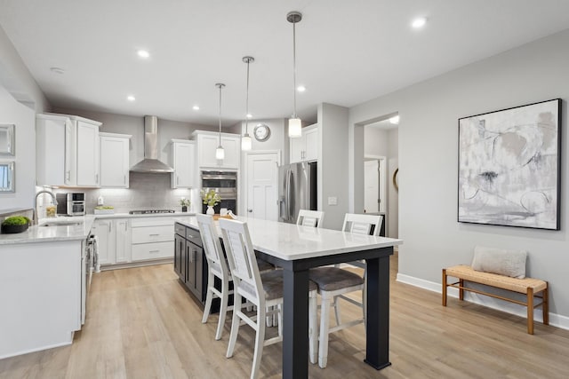 kitchen with appliances with stainless steel finishes, decorative light fixtures, a kitchen island, wall chimney exhaust hood, and white cabinets