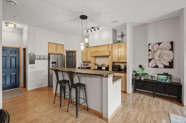 kitchen featuring stainless steel appliances, a kitchen island with sink, hanging light fixtures, and light brown cabinets