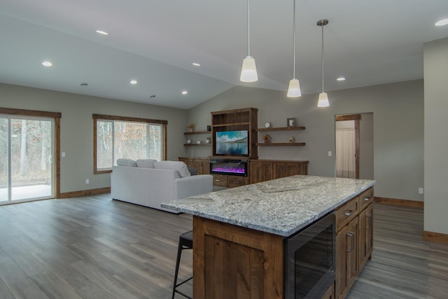 kitchen with light stone countertops, vaulted ceiling, a center island, decorative light fixtures, and wine cooler