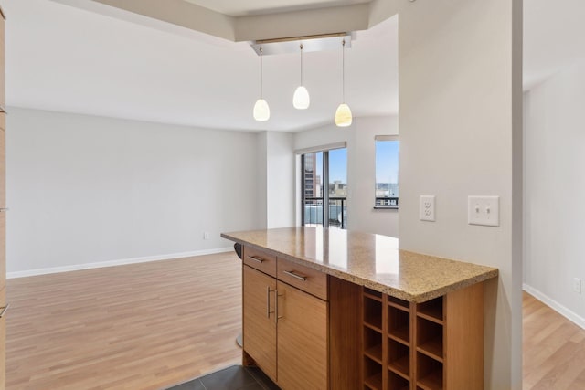 kitchen with wood-type flooring, light stone countertops, and pendant lighting