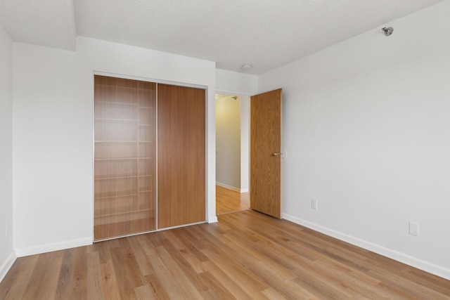 unfurnished bedroom featuring a textured ceiling, a closet, and light hardwood / wood-style flooring