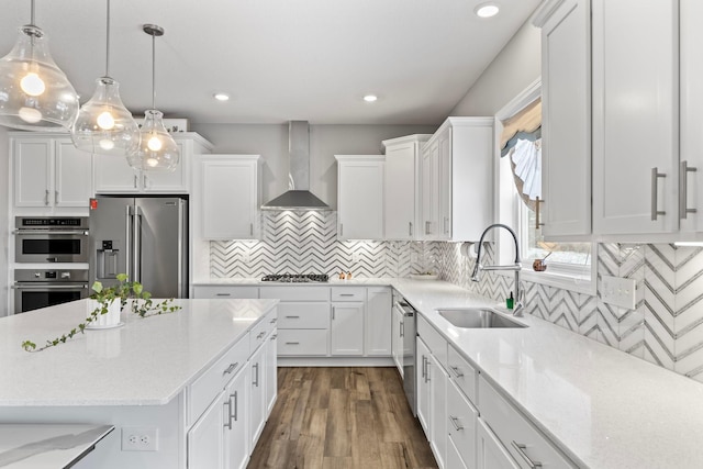 kitchen with sink, stainless steel appliances, wall chimney range hood, and white cabinetry