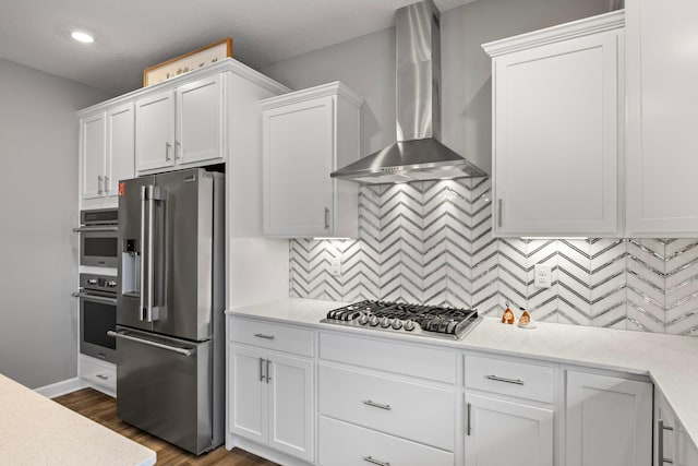 kitchen with white cabinets, appliances with stainless steel finishes, wall chimney exhaust hood, and hardwood / wood-style floors