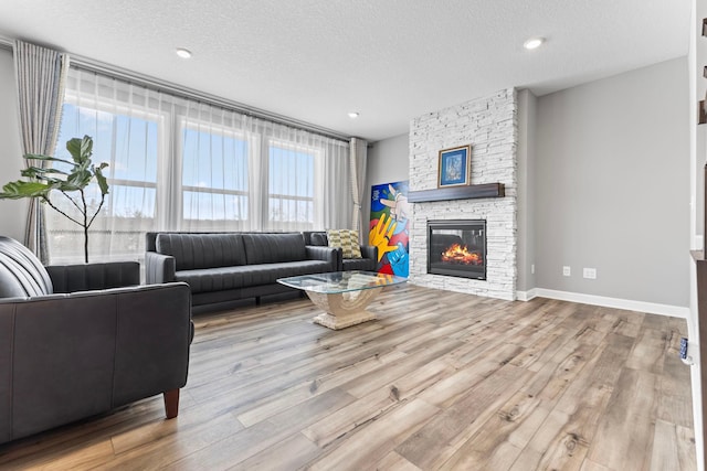 living room with a textured ceiling, light hardwood / wood-style floors, and a stone fireplace