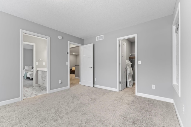 unfurnished bedroom featuring light colored carpet, a textured ceiling, connected bathroom, and a spacious closet