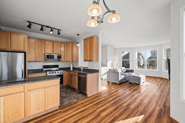 kitchen with appliances with stainless steel finishes, sink, dark hardwood / wood-style flooring, dark stone counters, and hanging light fixtures