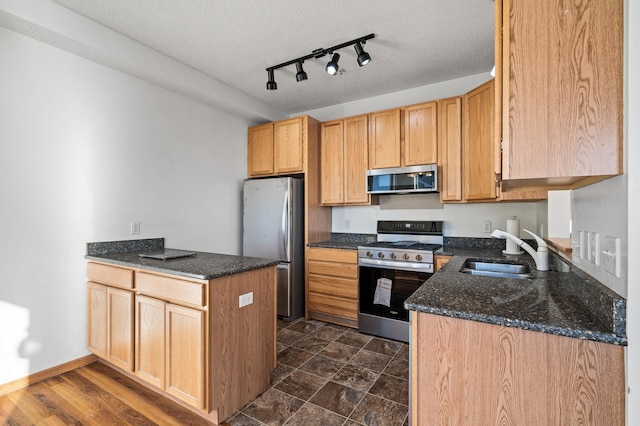 kitchen with stainless steel appliances, sink, a textured ceiling, and dark stone countertops