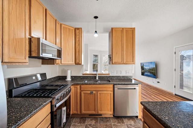 kitchen featuring appliances with stainless steel finishes, sink, hanging light fixtures, and dark stone countertops