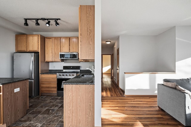 kitchen featuring sink, dark stone countertops, dark hardwood / wood-style flooring, stainless steel appliances, and a textured ceiling