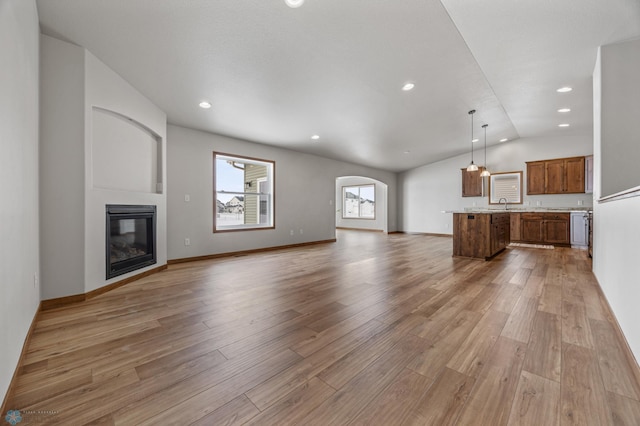 unfurnished living room with lofted ceiling, light hardwood / wood-style flooring, and sink