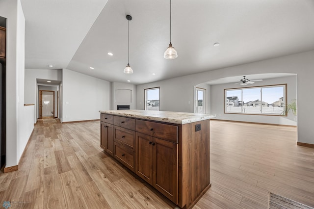 kitchen with light hardwood / wood-style floors, ceiling fan, light stone countertops, pendant lighting, and a center island