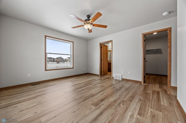 unfurnished bedroom with ensuite bathroom, ceiling fan, light wood-type flooring, a closet, and a walk in closet