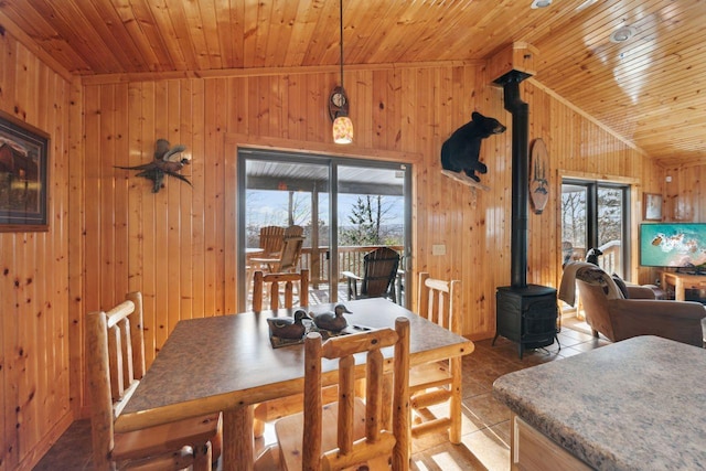 tiled dining area with wooden walls, lofted ceiling, and a wood stove