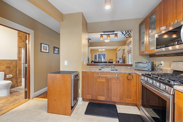 kitchen featuring appliances with stainless steel finishes, brown cabinetry, glass insert cabinets, and a sink