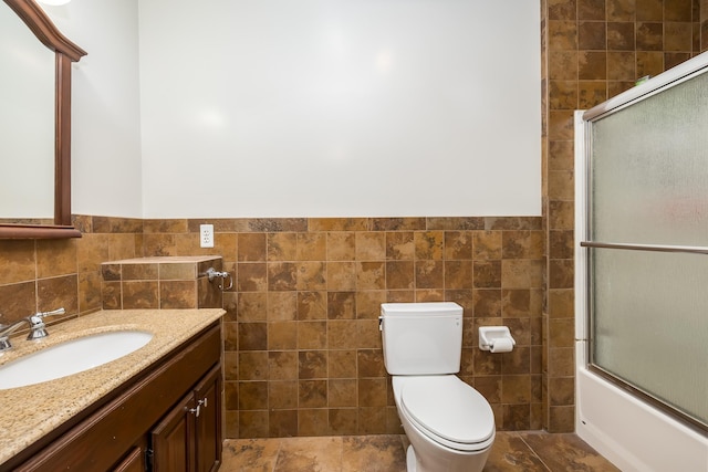 bathroom featuring toilet, combined bath / shower with glass door, tile walls, and vanity